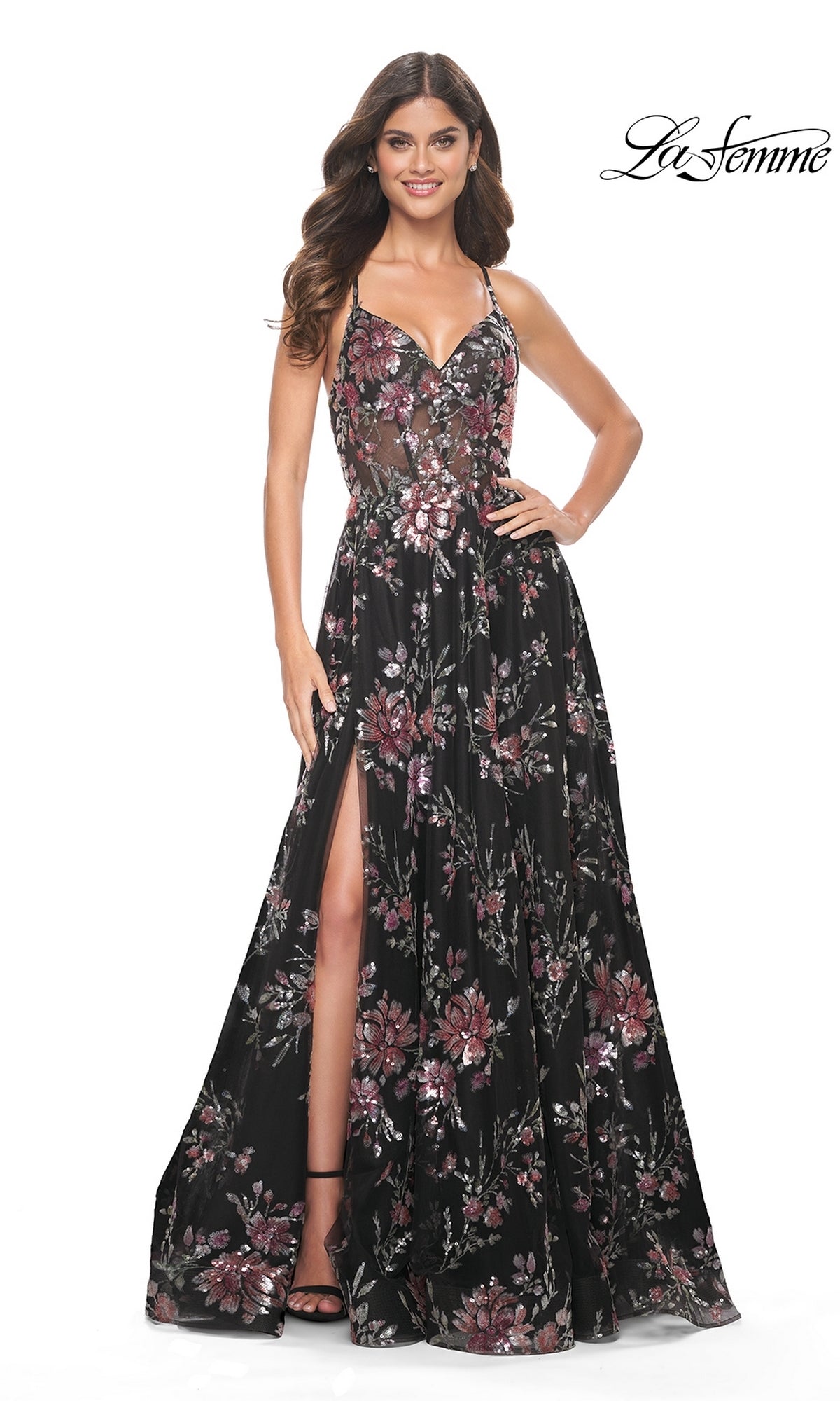 A woman stands smiling against a white background in the La Femme Floral-Sequin Long A-Line Prom Dress 32031, featuring black fabric, spaghetti straps, sequin floral detailing, a high slit, and a fitted bodice.